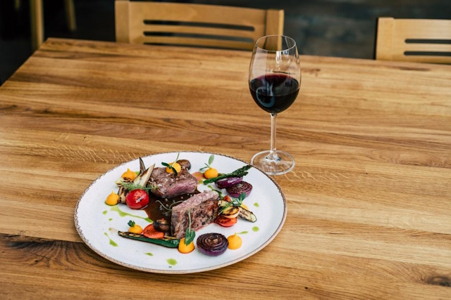 Steak artfully plated with spring vegetables on a table with a glass of red wine